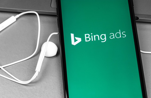 Bing Ads white text on green background on phone screen with ear bud adjacent