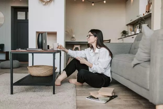 Woman sitting on floor in front of couch using laptop on coffee table